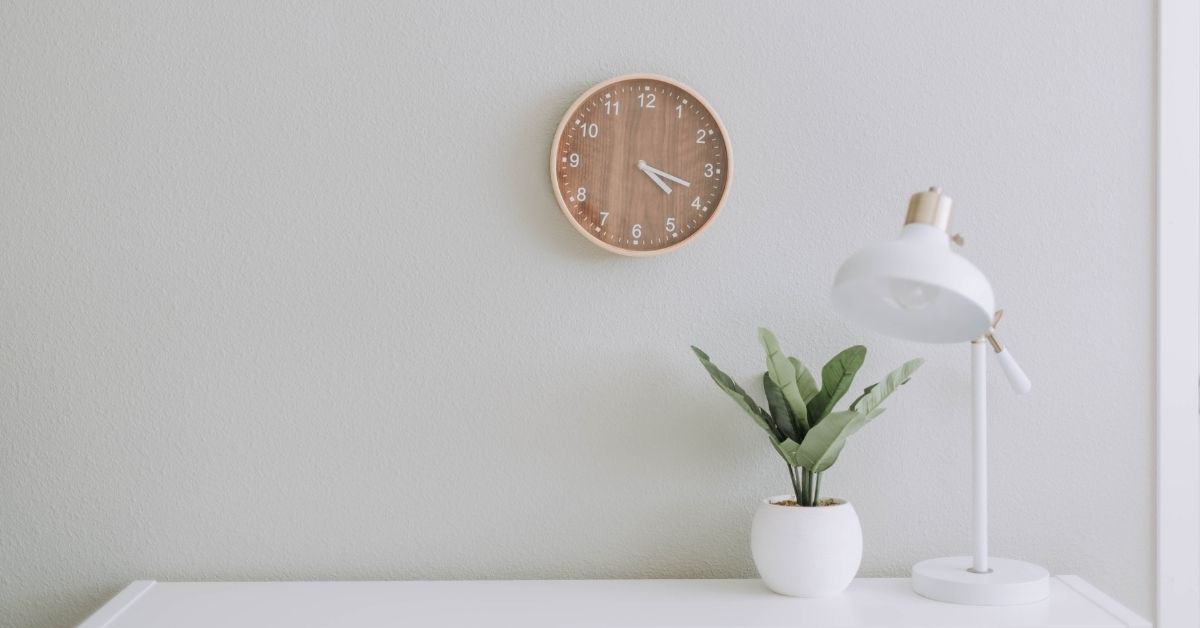 a minimalistic fresh white workspace with a clock, plant, desk and lamp