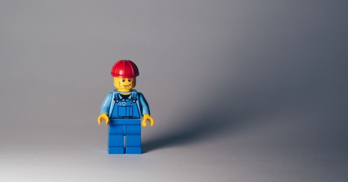 a lego man in blue overalls and a red hard hat