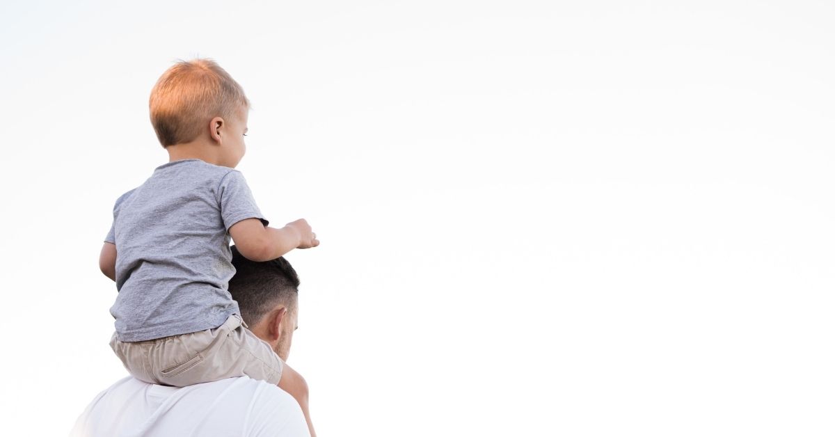 a boy sits on his father's shoulders
