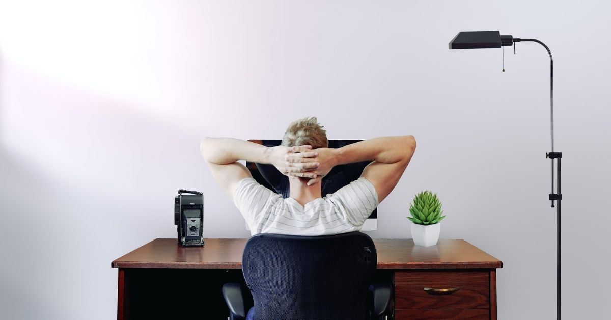 a person leans back in their chair with hands behind head, working from home