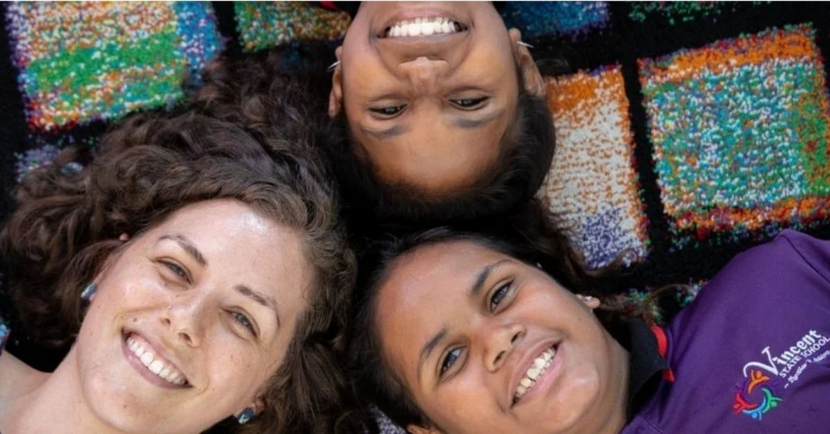 three girls laying on the ground smiling with heads together
