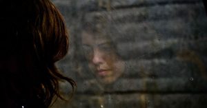 woman looking sad at reflection in glass