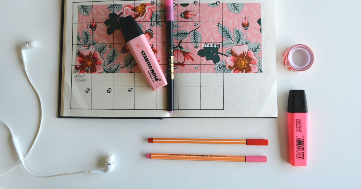 A diary on a desk with pink highlighters and pens