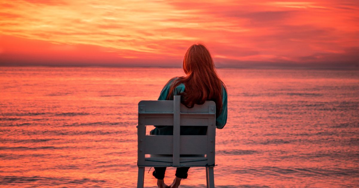 Woman sitting on beach at sunrise