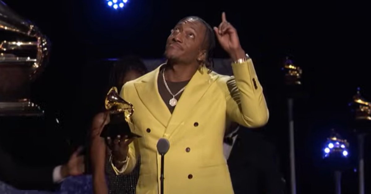 Artist Lecrae in bright yellow suit points and looks to heavens as accepts Grammy award