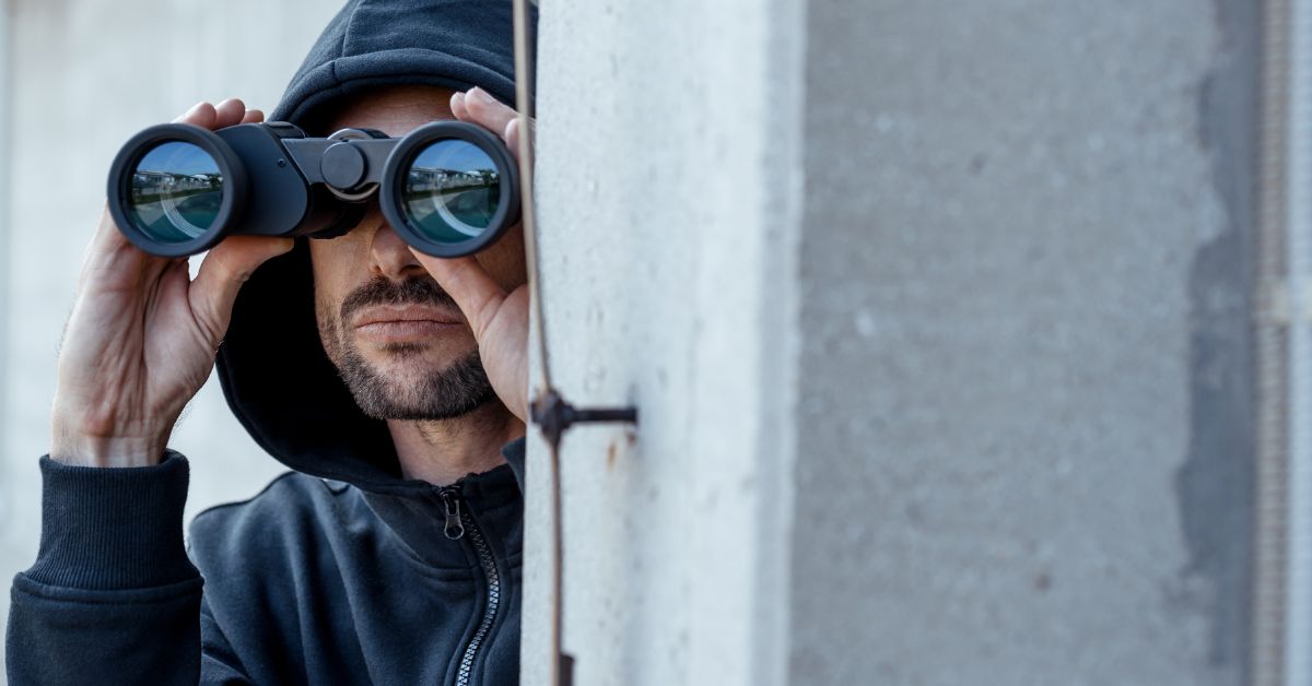 A man in dark hoodie with binoculars