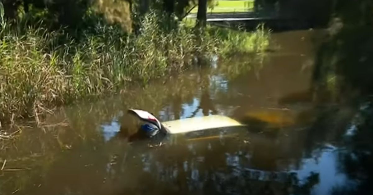 car submerged in creek with only roof visible and boot open