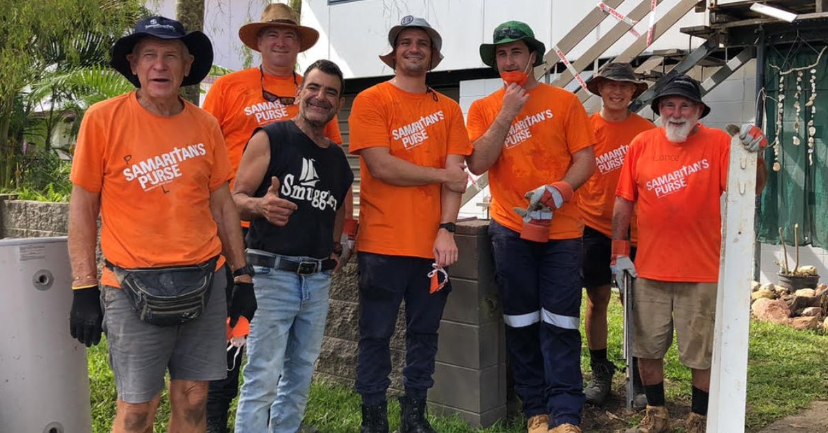 Volunteers in bright orange shirts with tools in clean up of flood affected area